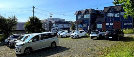 Un estacionamiento con varios autos y un edificio de fachada oscura y múltiples ventanas.