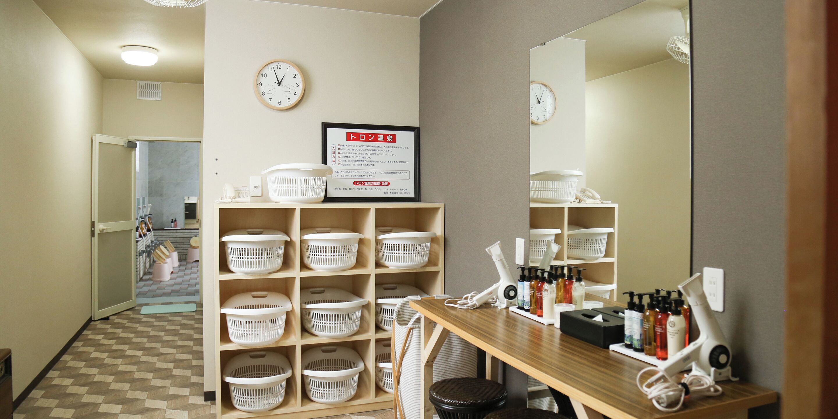 A hotel bathroom with a mirror, a clock, and shelves with baskets and toiletries.