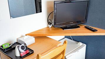 Ein Hotelzimmer mit Fernseher auf einem Holztisch, einer Fernbedienung, einer Kamera und einem Tablett mit einer Kaffeetasse und einer Schachtel.
