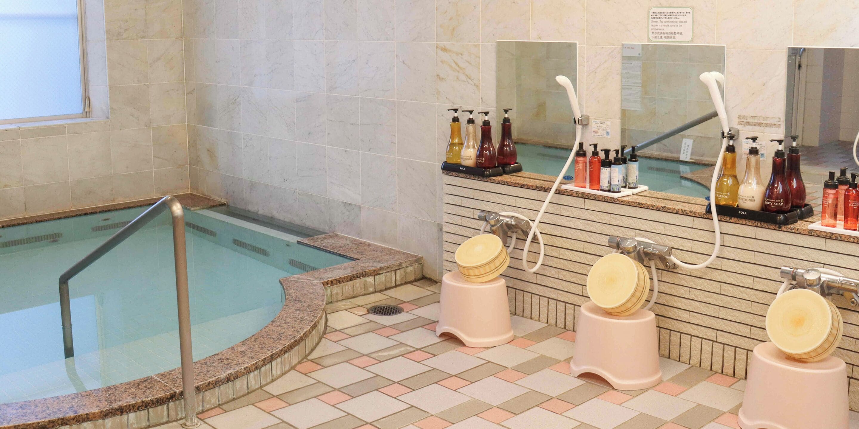 Zona de spa con bañera de hidromasaje, regaderas y varios artículos de aseo en dispensadores.