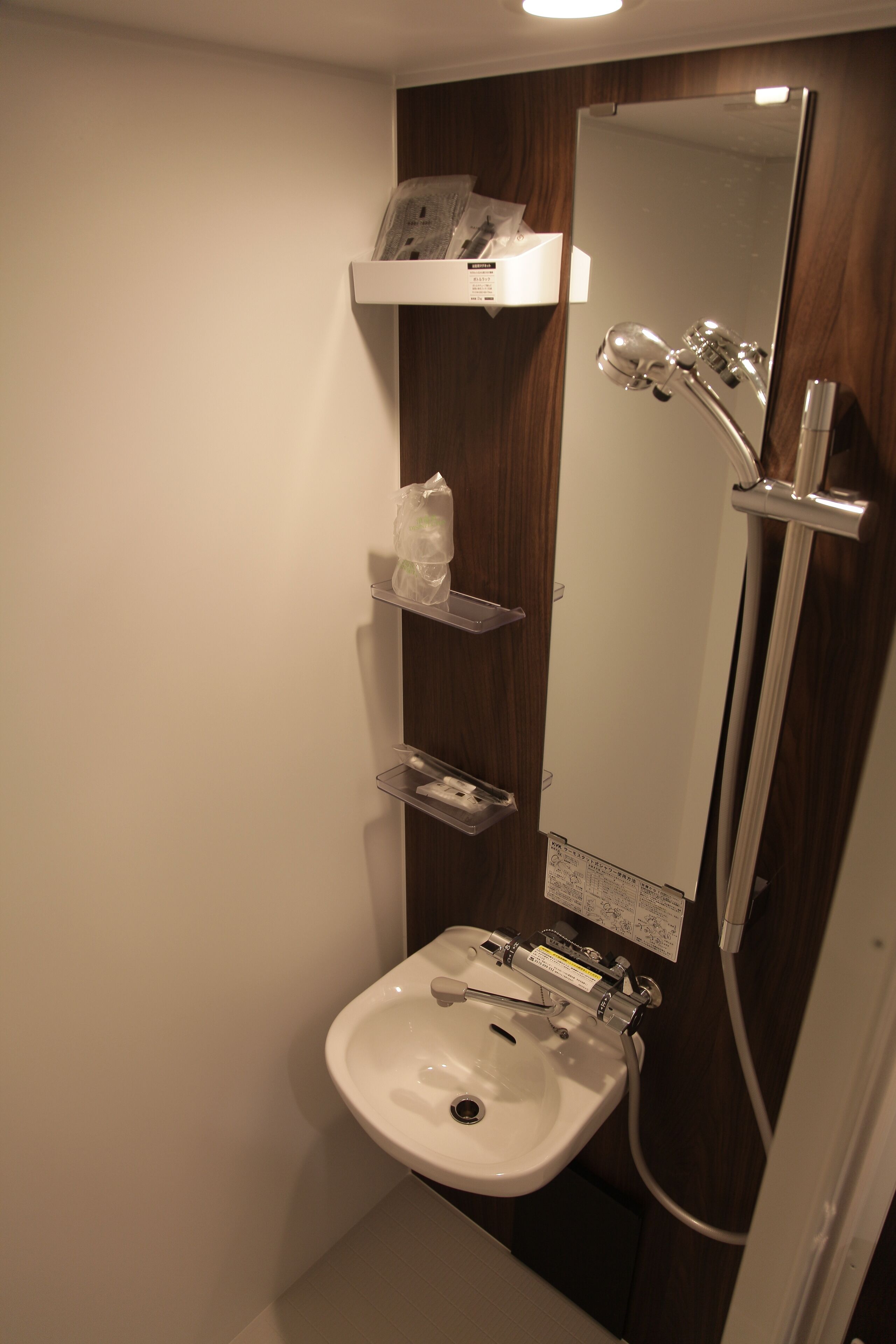 A bathroom with a white sink, a mirror, and a shower. There are shelves above the sink and a towel rack.