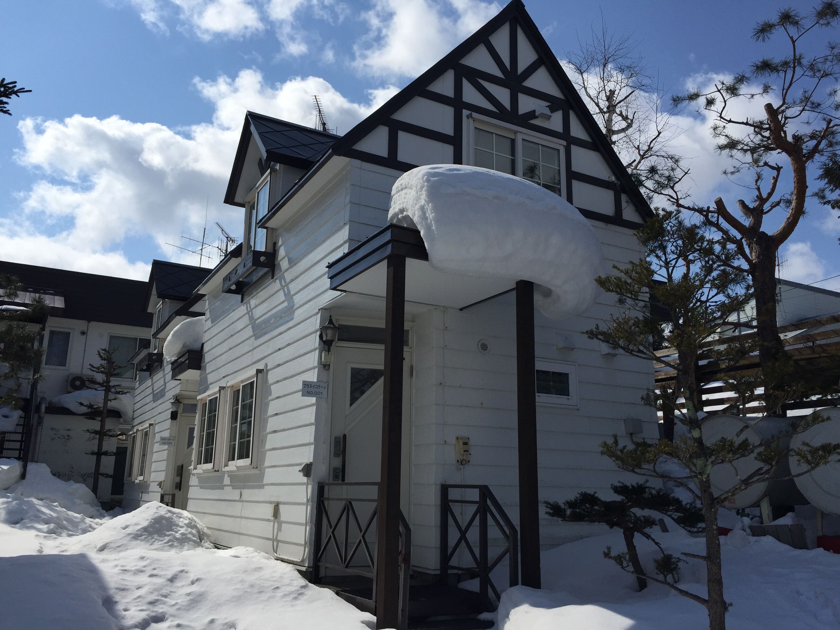 A white house with a steeply pitched roof, surrounded by snow.
