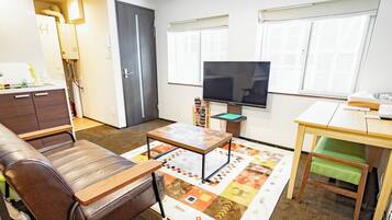 A living room with a sofa, a coffee table, a TV, and a small table with a chair.