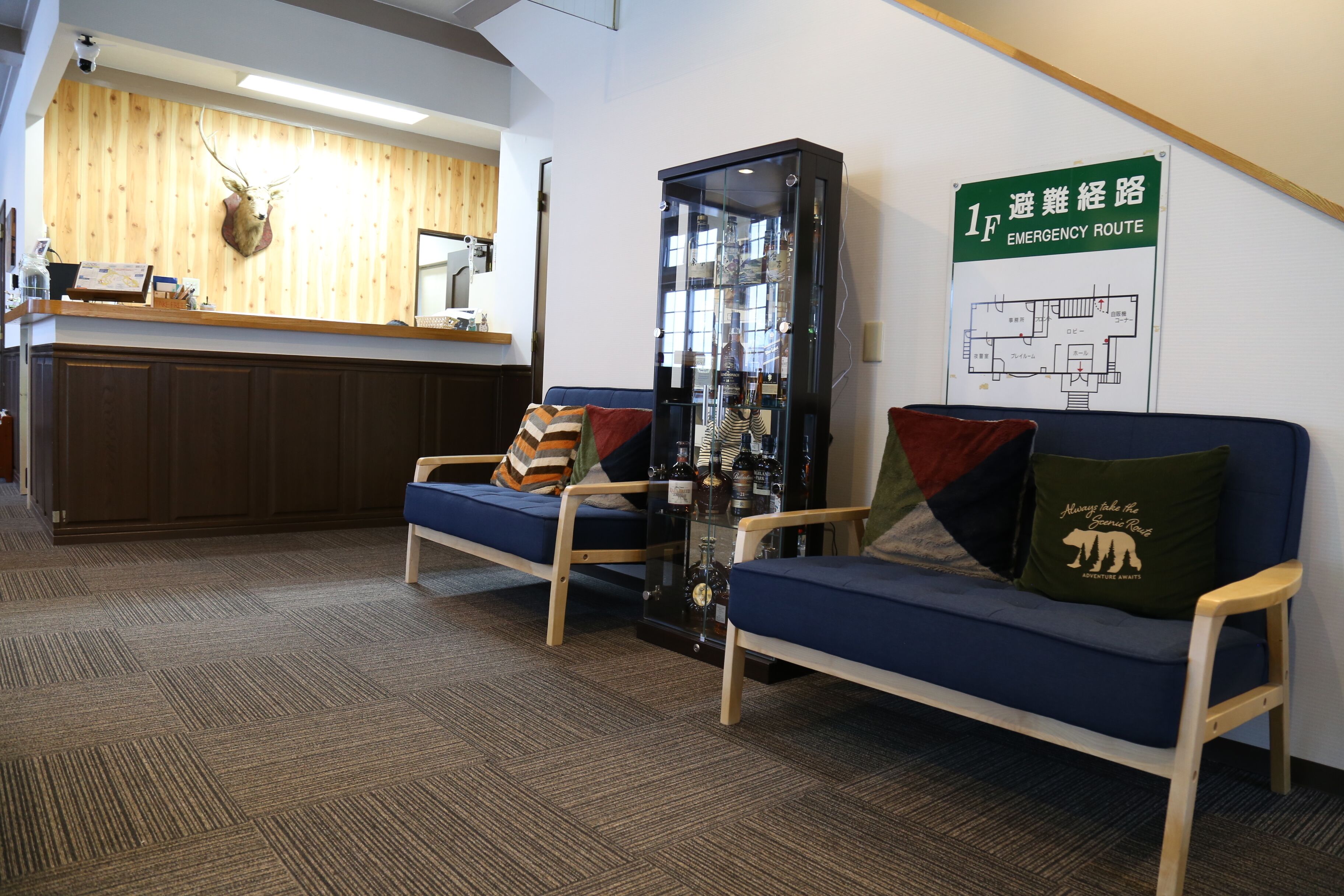 A reception area with a wooden wall, a mounted deer head, a reception desk, a glass display cabinet, and a blue sofa with a pillow.