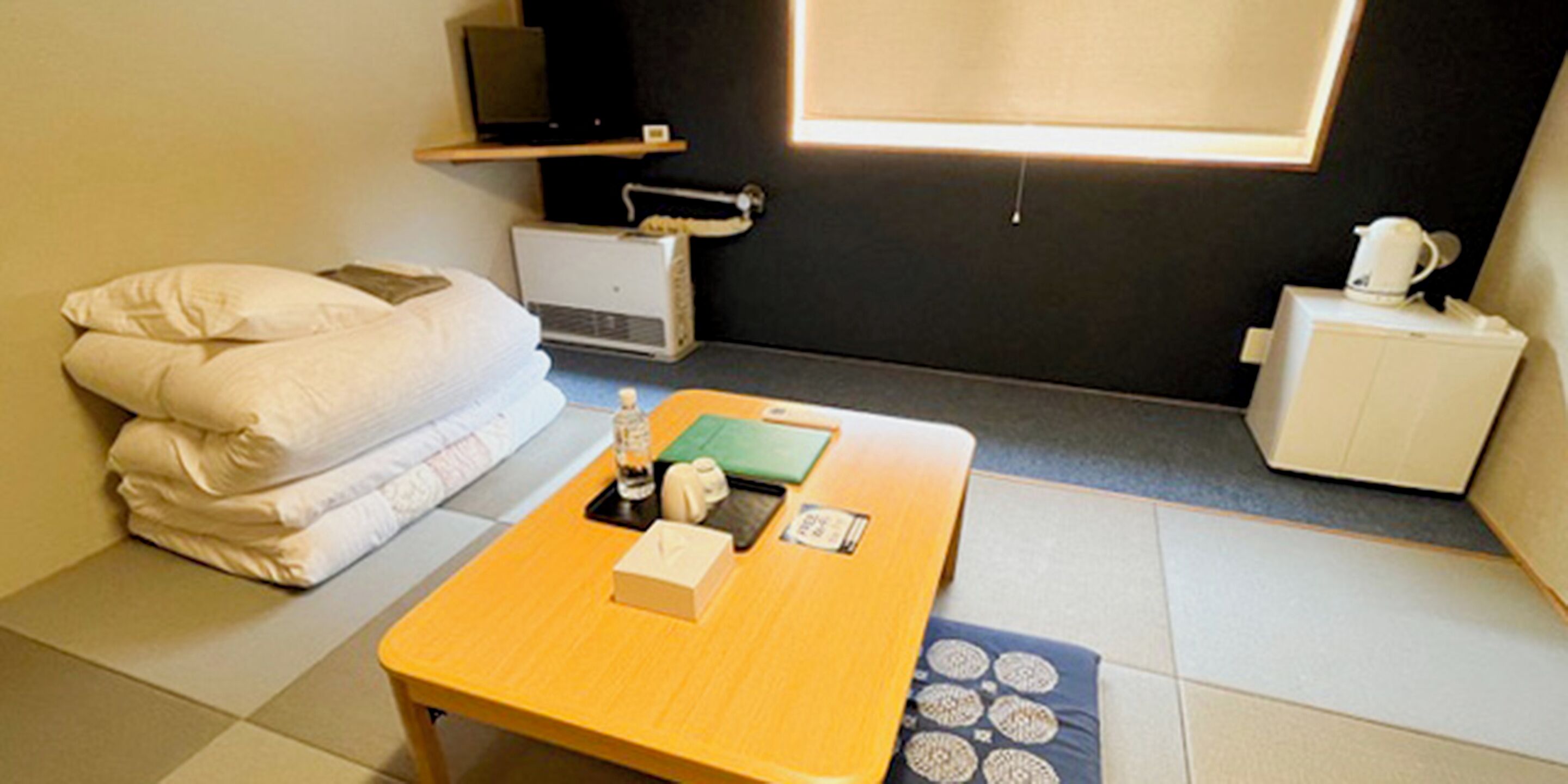 Habitación de hotel compacta con una cama, un escritorio pequeño con una computadora portátil, una cafetera y un televisor sobre una repisa.