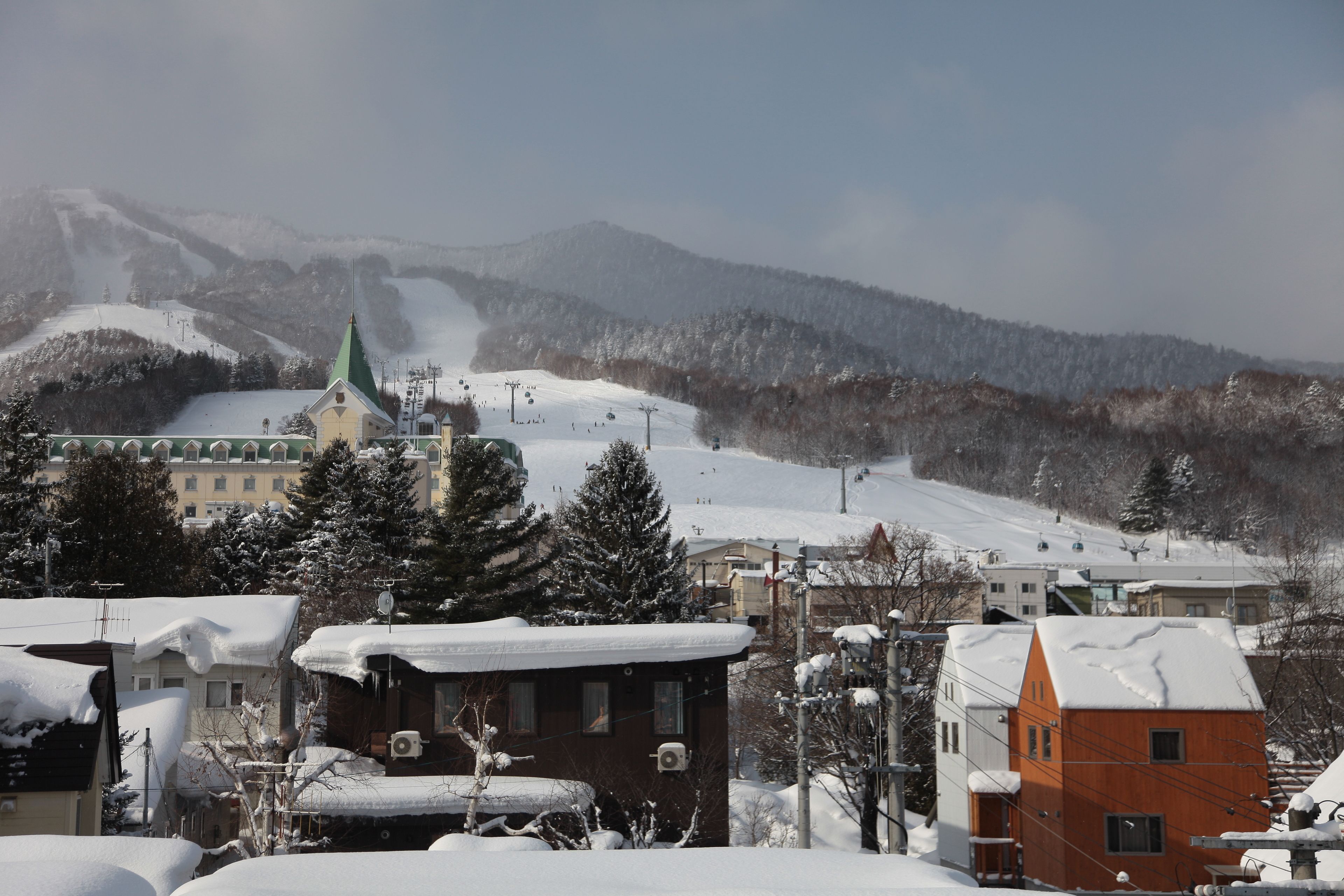 A snow-covered town with a church, houses, and a ski slope in the background.
