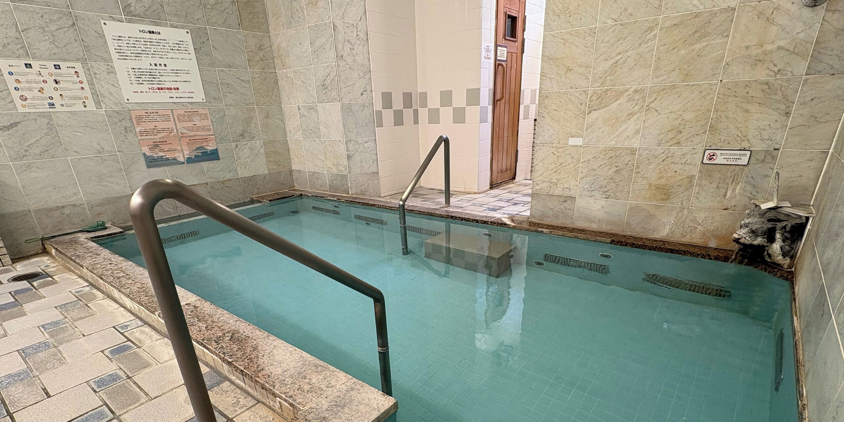A swimming pool with tiled walls and a metal handrail.