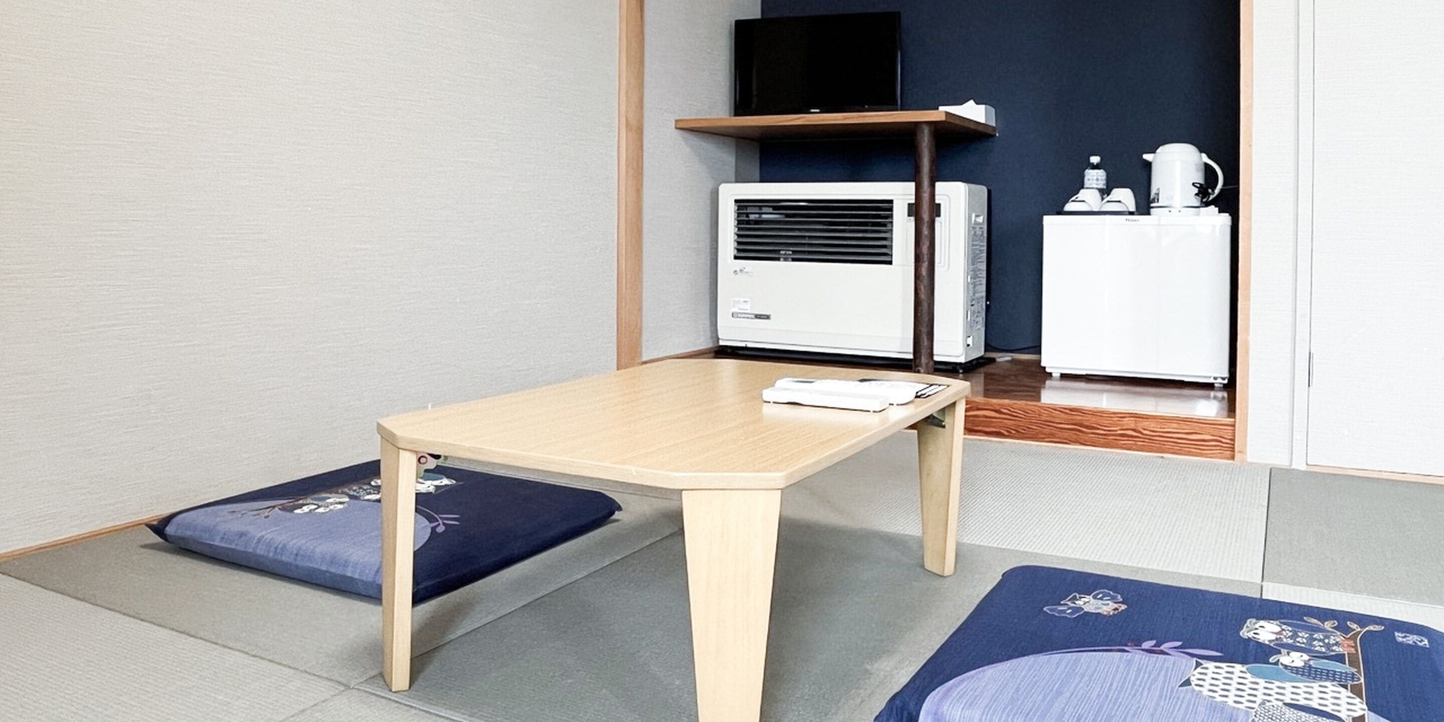 Una habitación con una mesa de madera, dos cojines azules, un equipo de aire acondicionado blanco y un refrigerador blanco.
