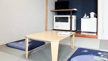 Una habitación con una mesa de madera, dos cojines azules, un equipo de aire acondicionado blanco y un refrigerador blanco.