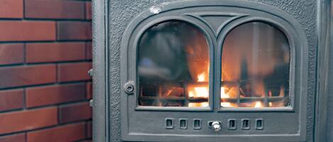 A wood-burning stove with a glass door, set against a brick wall.