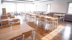 Une salle de classe spacieuse, avec des tables et des chaises en bois, de grandes fenêtres et un radiateur le long du mur.
