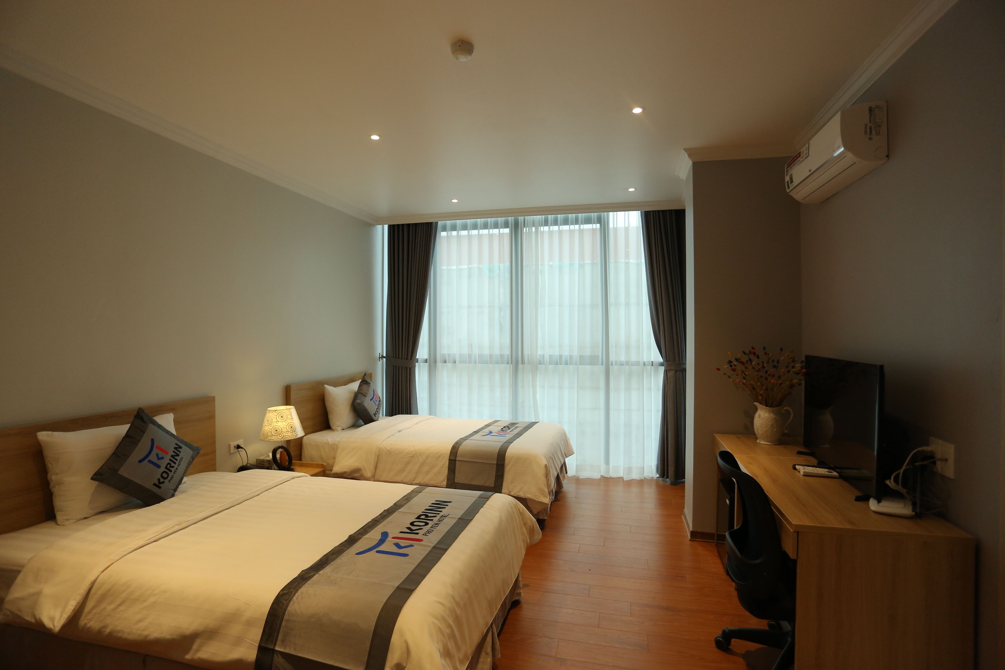 Een hotelkamer met twee bedden, een bureau met een computer en een raam met gordijnen.
