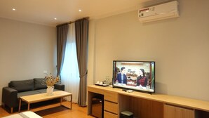A modern living room with a sofa, a coffee table with a vase, a TV on a wooden stand, and an air conditioner on the wall. - Korinn Pho Yen Hotel (Van Xuan)