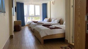 A hotel room with two beds, a wooden floor, a small stool, and a window with curtains. - Van Minh Hotel (Xuan Huong - Da Lat)