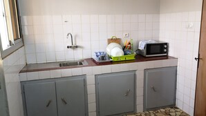Une petite cuisine équipée d’un évier, d’un four à micro-ondes et d’un égouttoir à vaisselle. On y trouve des placards sous le plan de travail et une fenêtre sur le côté gauche.