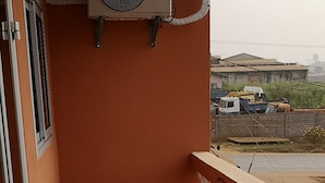 Un balcon doté d’un climatiseur Samsung, d’un sol carrelé et offrant une vue sur un chantier de construction en arrière-plan.