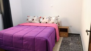Une petite chambre à coucher, bien rangée, avec un lit, une table de chevet et une commode en bois.