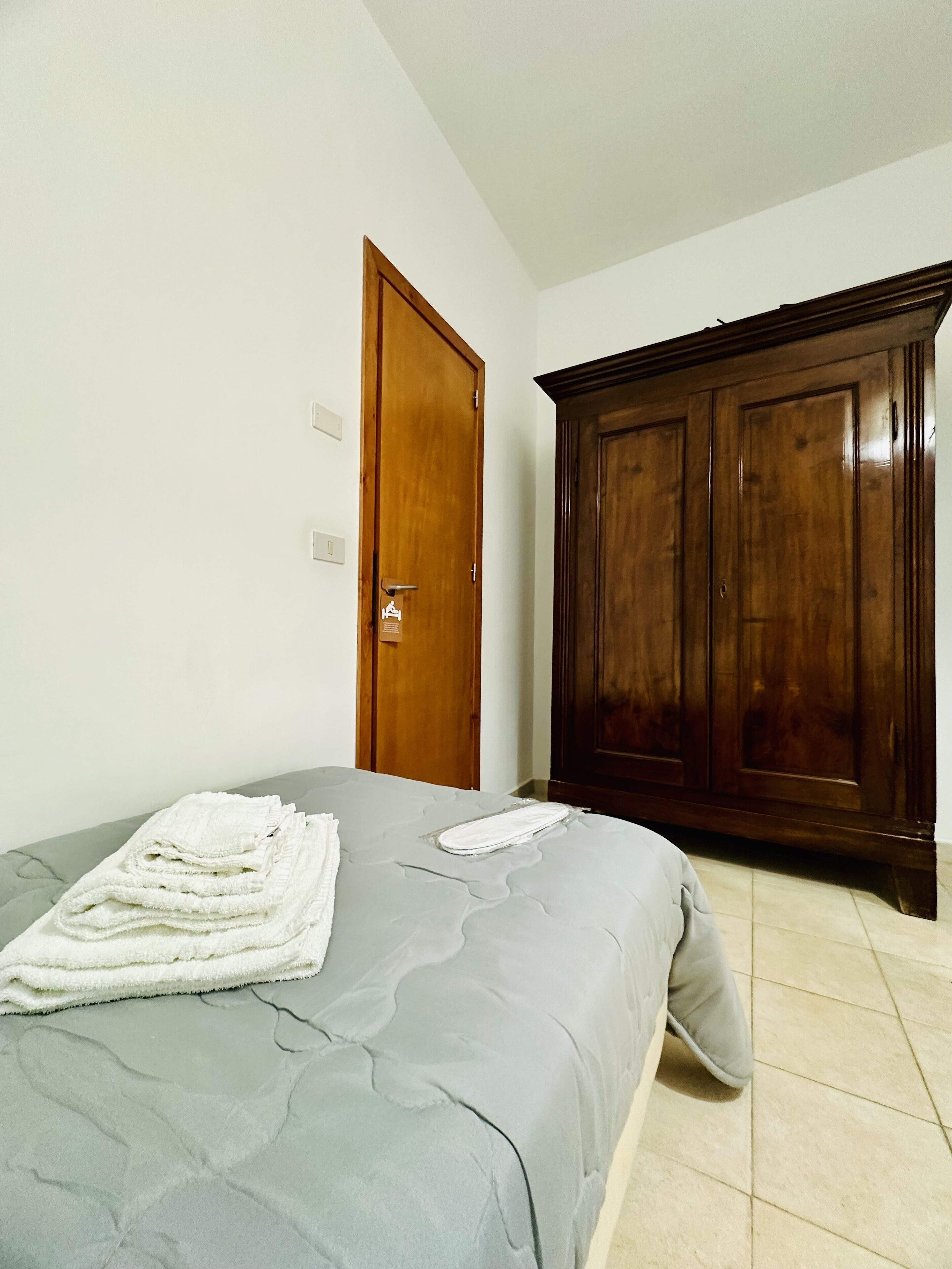 A bedroom with a bed, a wooden wardrobe, and a door.