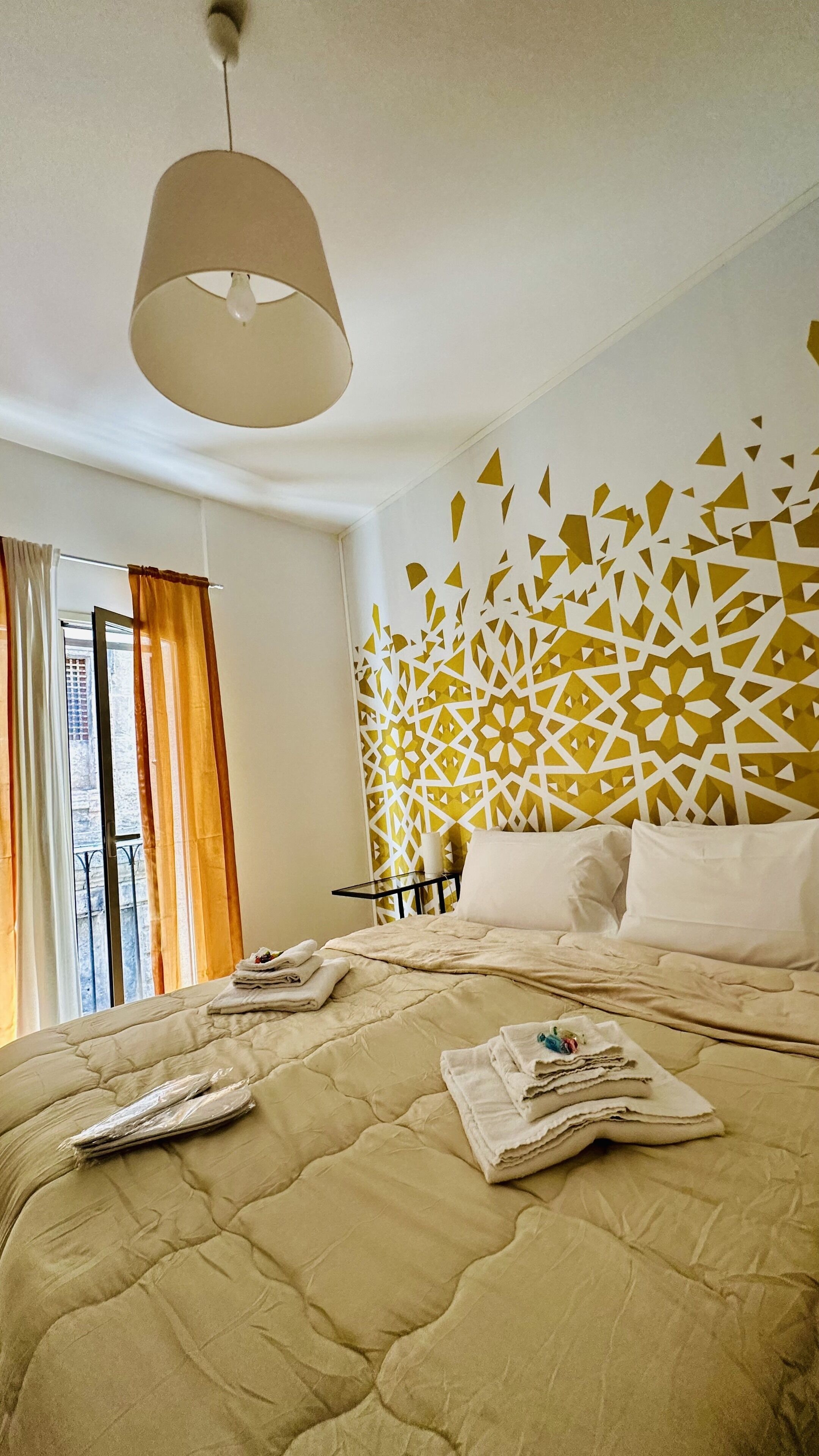 Habitación de hotel con cama, lámpara de techo, pared con diseño y vista al exterior.