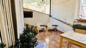 Ein Patio mit Fliesenboden, einem Holztisch, zwei weißen Stühlen und Topfpflanzen.