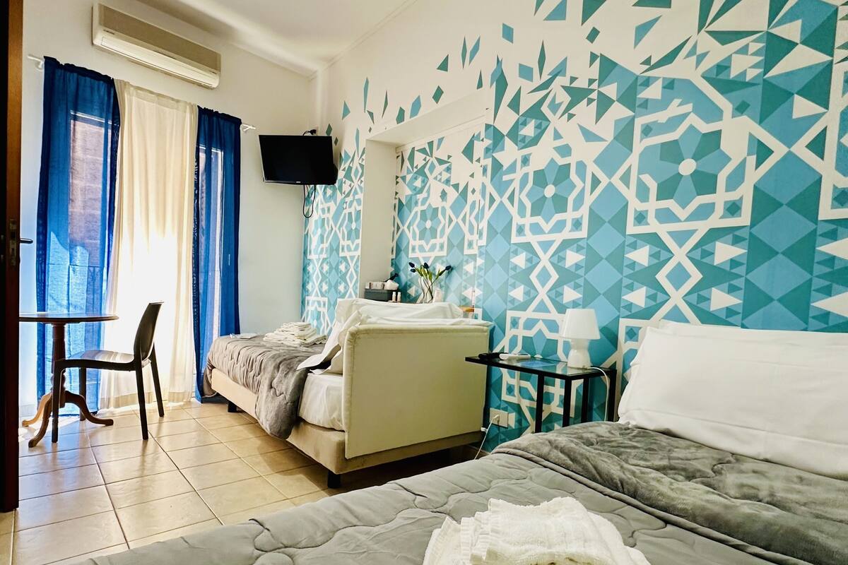 Una habitación de hotel con cama, escritorio, silla, televisor y pared con diseño.