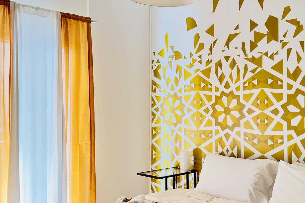 Una cama bien hecha con edredón color beige, una lámpara colgante y un panel decorativo en la pared.