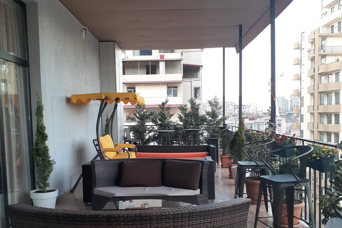 A balcony with wicker furniture, potted plants, and a view of surrounding buildings.