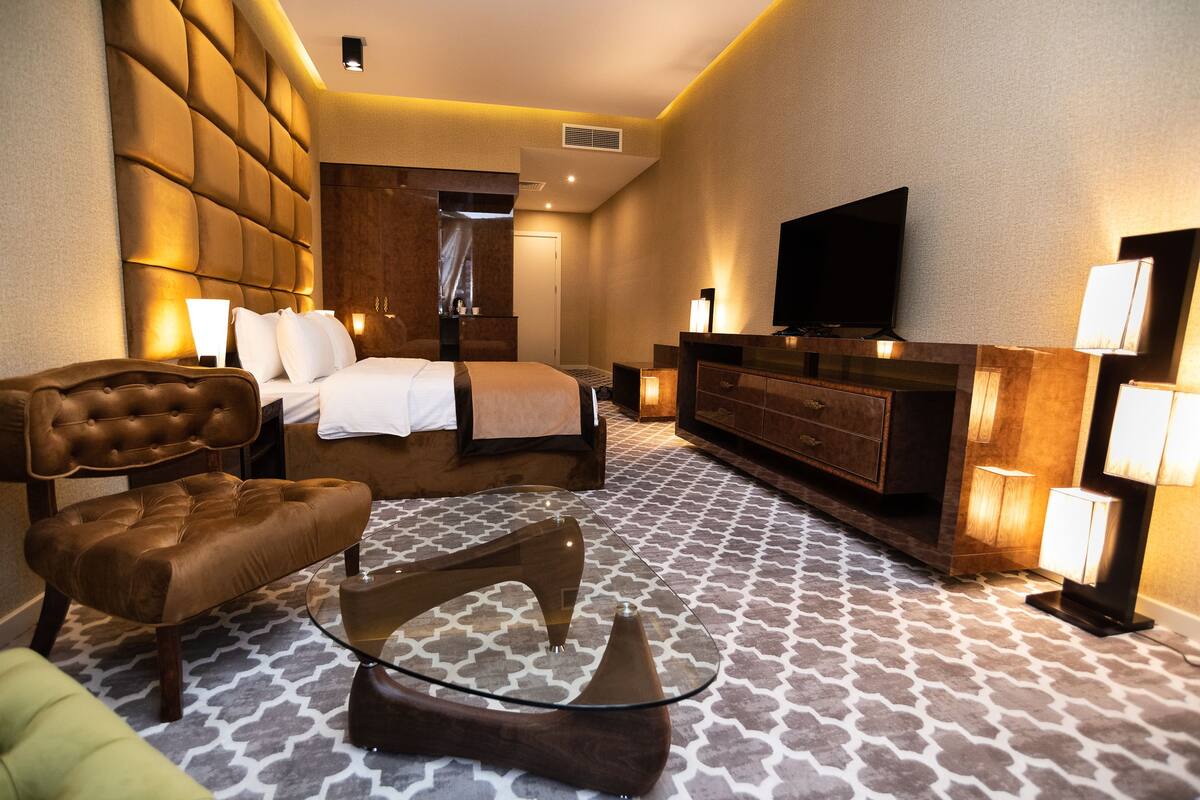 A hotel room with a large bed, a sofa, a glass coffee table, a TV, and a dresser.
