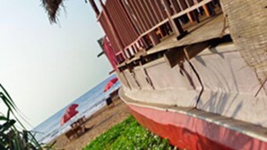 Un edificio frente a la playa con fachada roja y blanca, techo de paja y vista al océano.