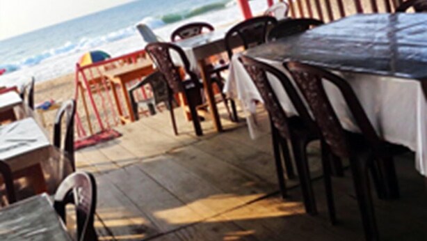 Un restaurante al aire libre con mesas y sillas de madera, con vista a la playa y al océano.