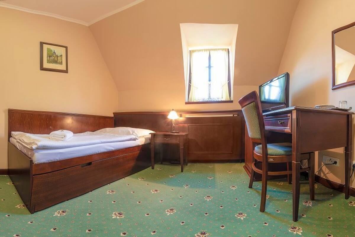 A bedroom with a bed, desk, chair, and a window with curtains.