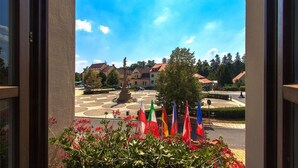 Une vue depuis une fenêtre donnant sur une cour intérieure avec une fontaine, entourée de bâtiments et d’arbres.