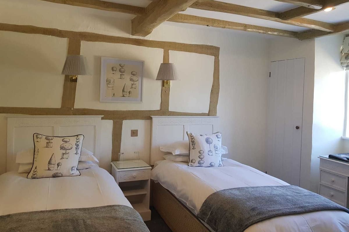 A bedroom with two beds, a nightstand, a wall-mounted lamp, and a door.