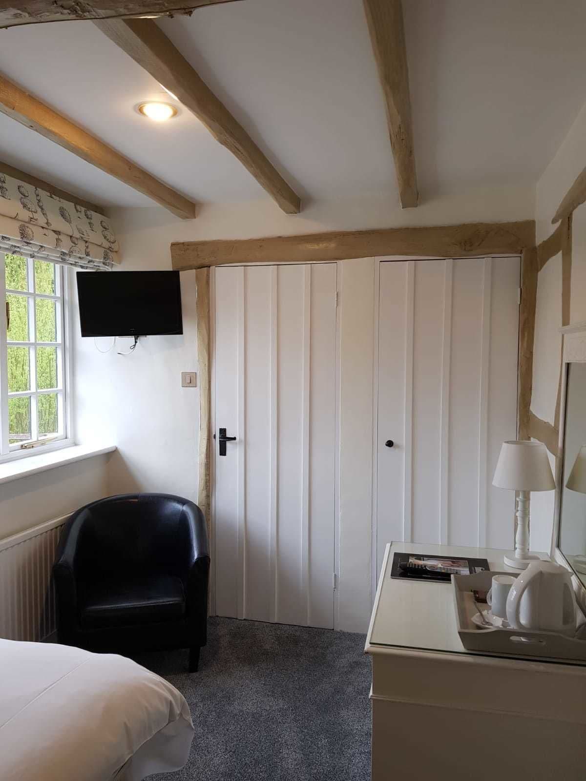 Una habitación con una cama, un sillón de cuero negro, un armario blanco, un televisor montado en la pared y una ventana con vista a la vegetación.