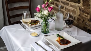 A dining table set with plates of food, wine glasses, cutlery, and a vase with flowers. - Random Hall Hotel (Horsham)