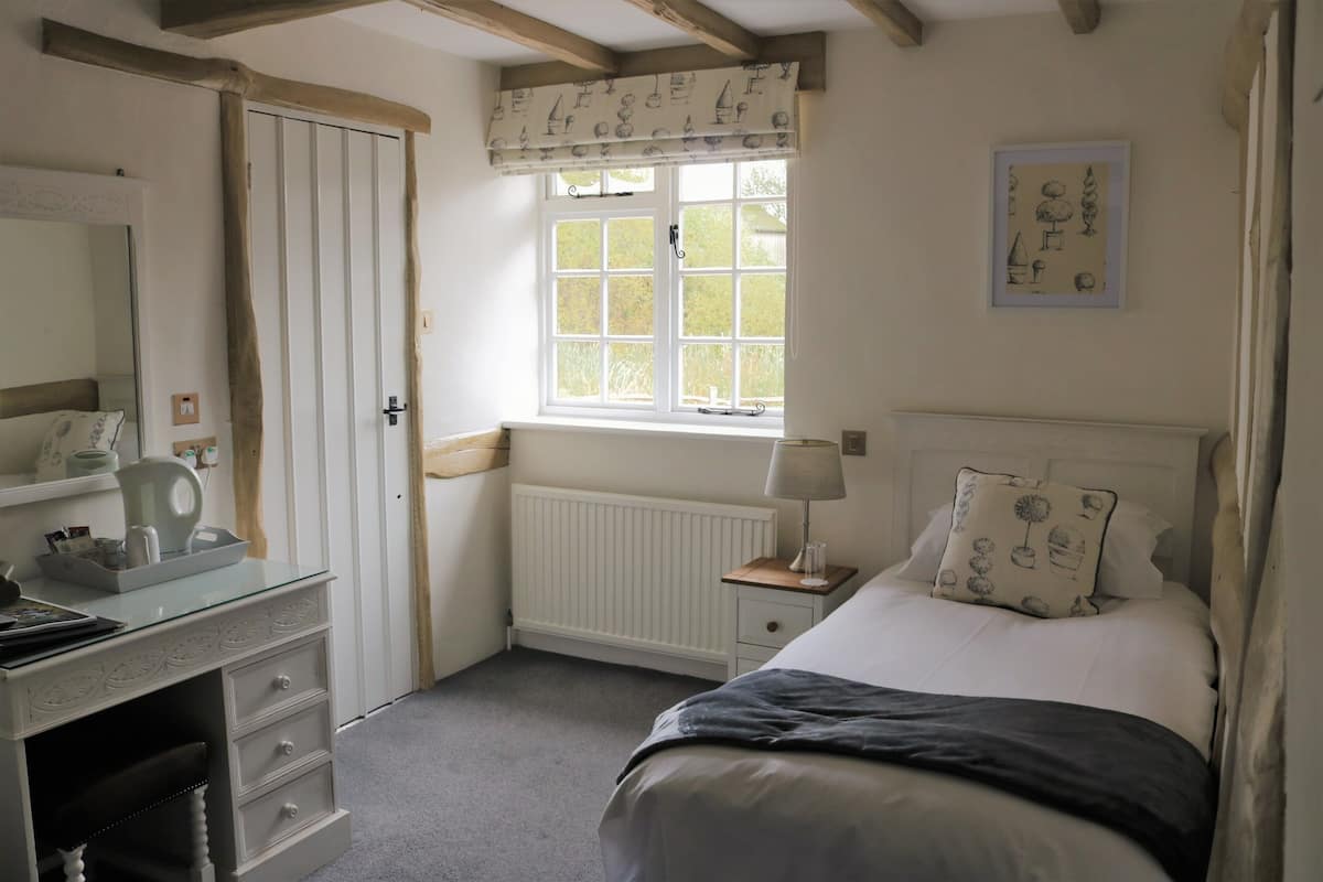 A bedroom with a bed, a dresser, a window with curtains, a radiator, and a framed picture on the wall.