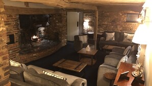 A cozy room with a brick fireplace, a sofa, a coffee table, and a lamp. - Random Hall Hotel (Horsham)