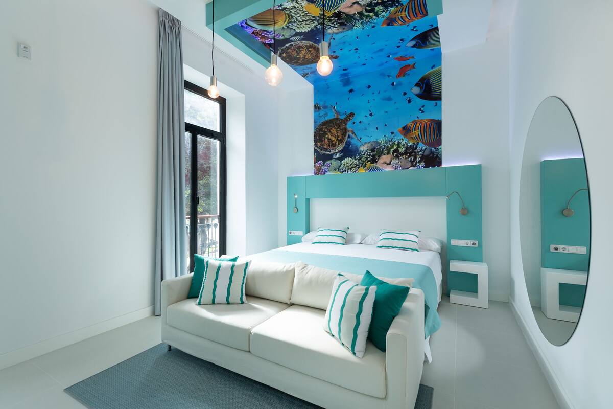 A modern bedroom with a bed, a sofa, a ceiling mural, and a large mirror.