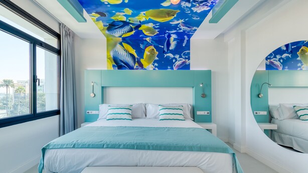 A modern hotel room with a large bed, a ceiling mural of tropical fish, and a view of palm trees. - HD Acuario Lifestyle (Las Palmas de Gran Canaria)
