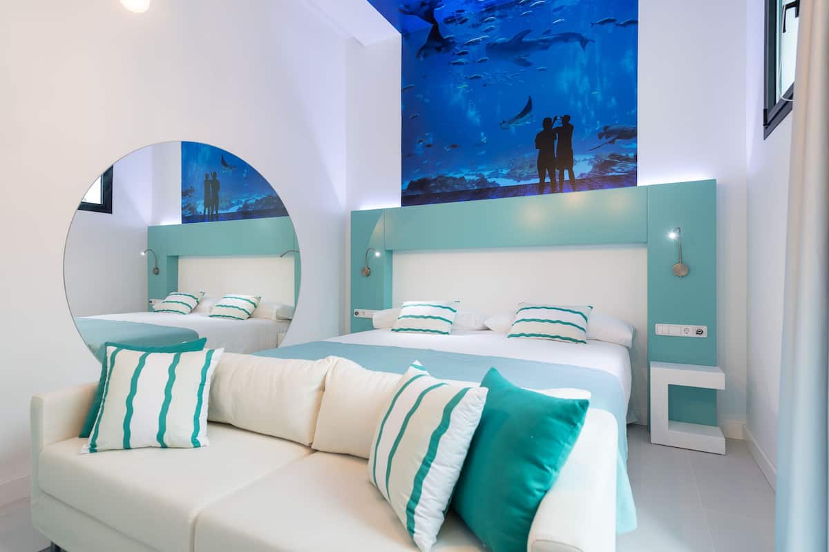 A modern bedroom with a large bed, a round mirror, and a wall mural of an underwater scene.