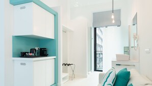 A modern, well-lit room with a kitchenette, a sofa with teal cushions, and a large window offering a view of the city. - HD Acuario Lifestyle (Las Palmas de Gran Canaria)