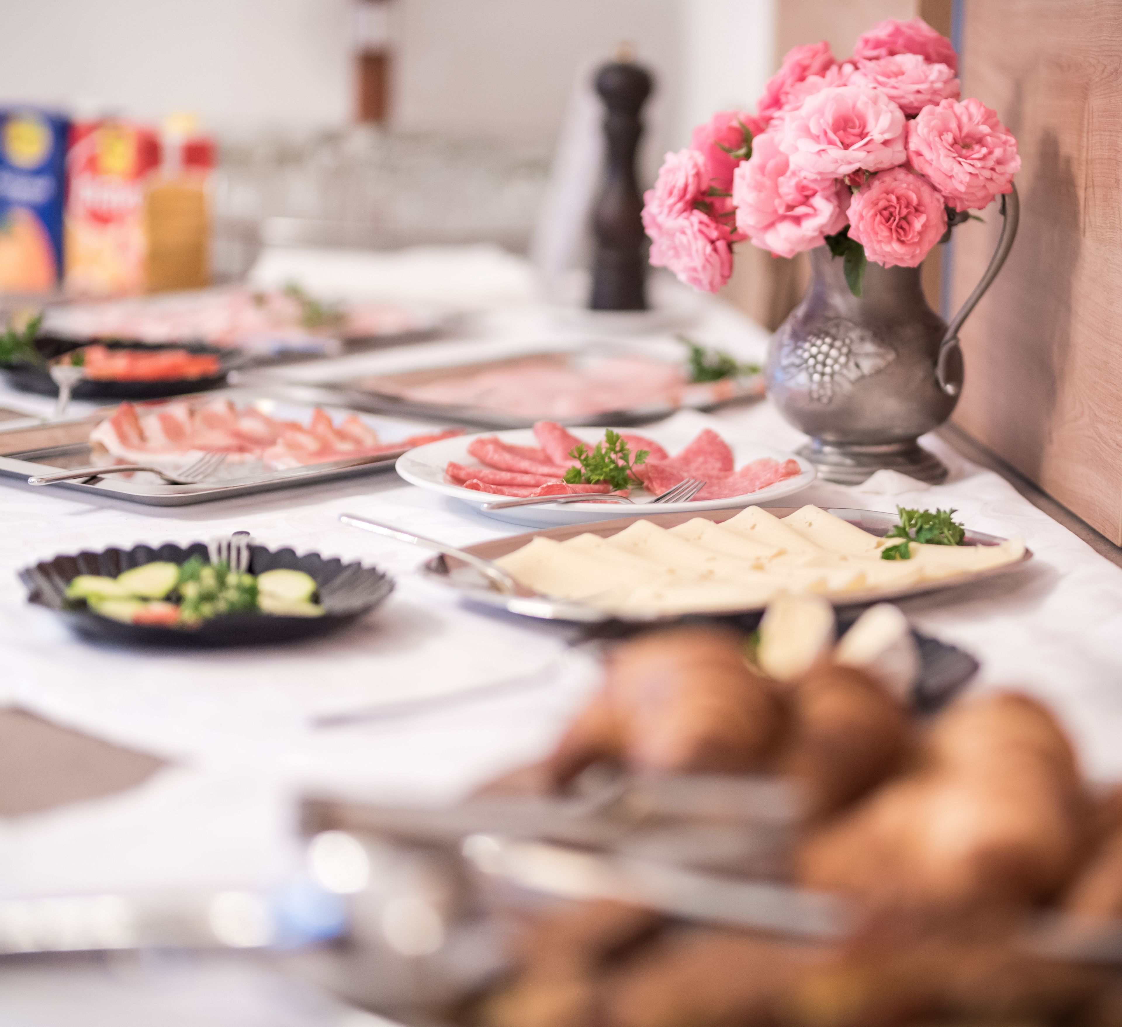 A buffet table with various food items and a vase of pink flowers.