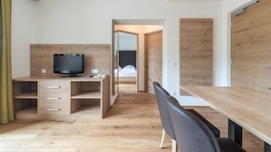 Un dormitorio moderno con un escritorio de madera, un televisor y una cama con ropa de cama blanca.