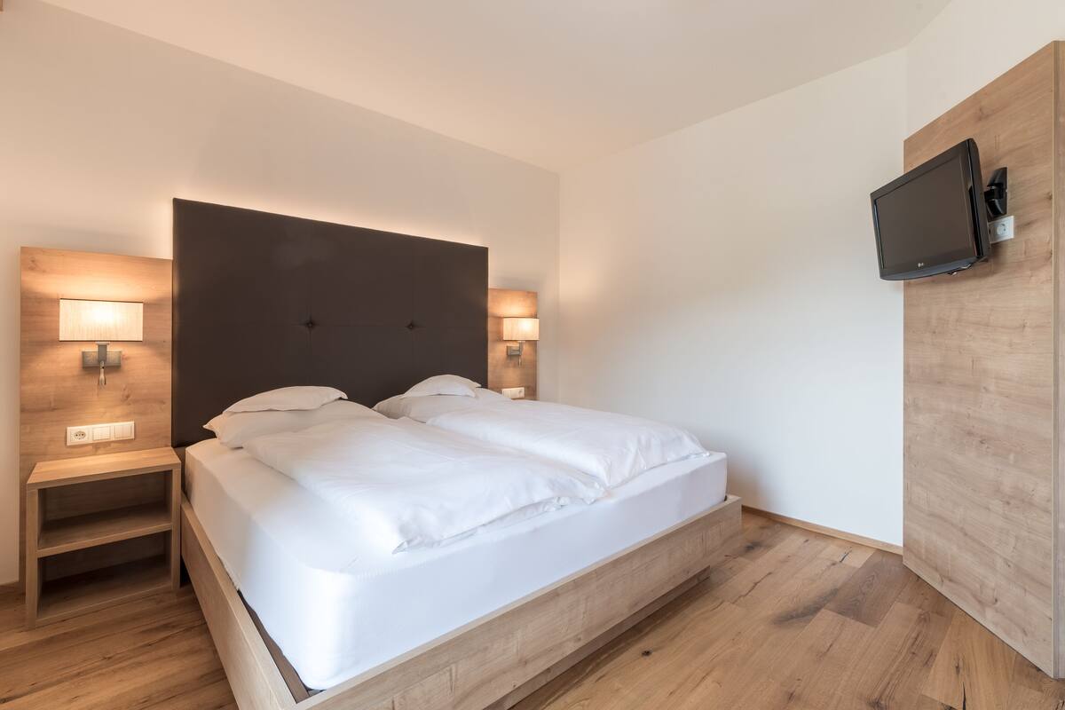 Ein modernes Hotelzimmer mit einem großen Bett, einem Holzkopfteil, Nachttischlampen und einem an der Wand befestigten Fernseher.