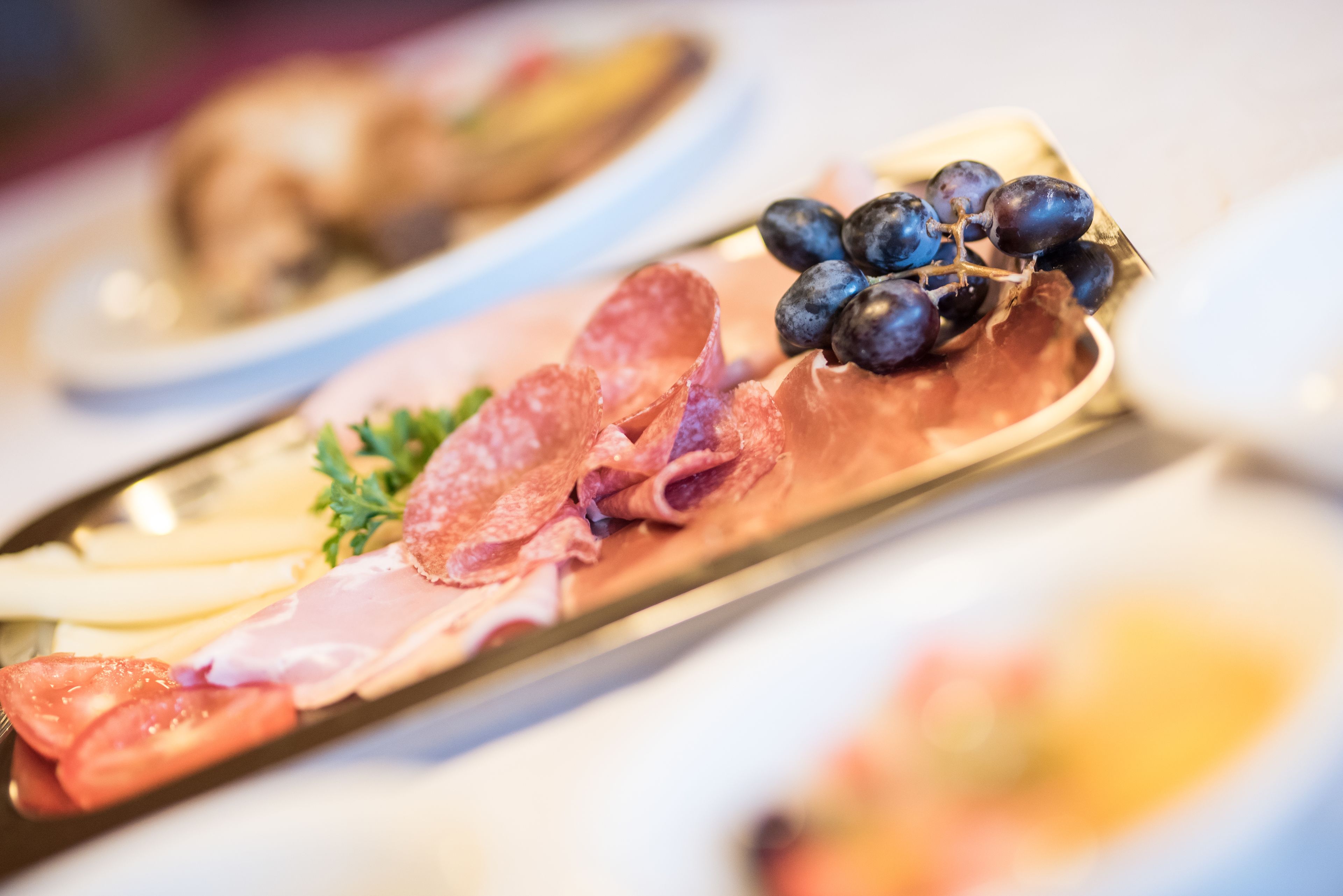 Una tabla de embutidos con diferentes carnes, queso y uvas.