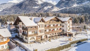 Un gran hotel de varios pisos con techo nevado y balcones, rodeado de montañas y árboles.
