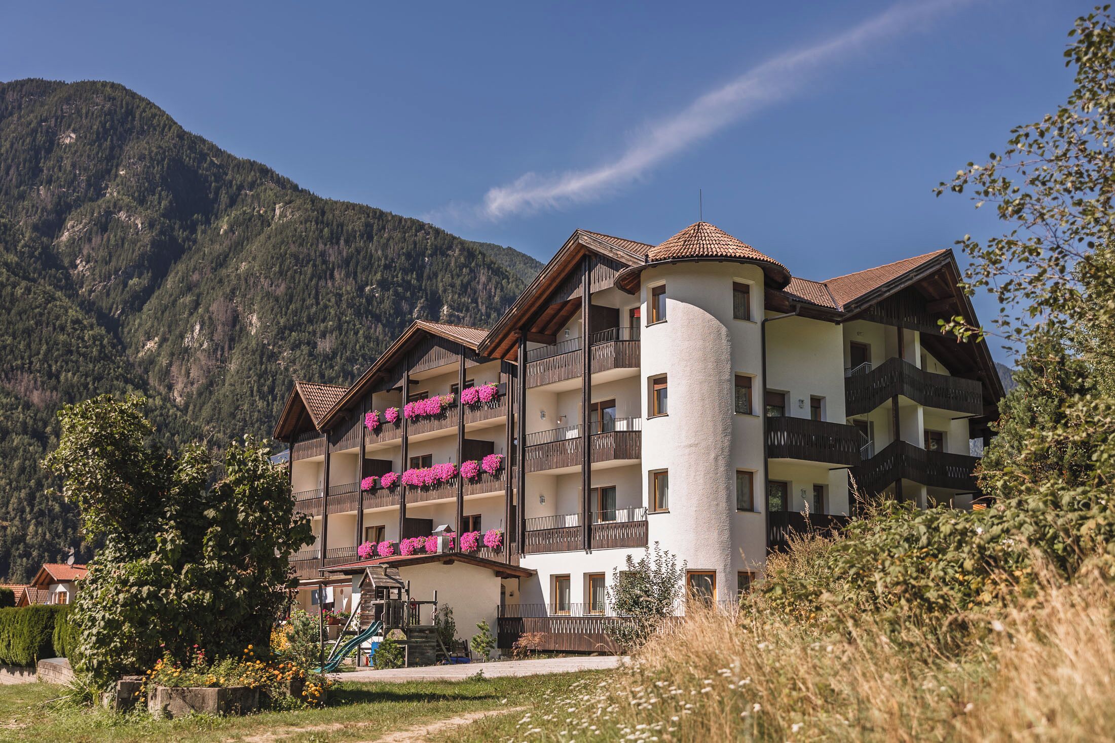 Un hotel de varios pisos con balcones, rodeado de montañas y vegetación.
