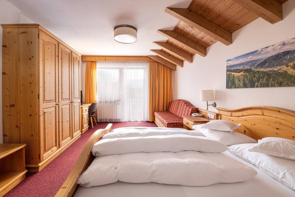 Ein Hotelzimmer mit einem großen Bett, einem Holzschrank, einem Schreibtisch und Blick auf eine Berglandschaft.