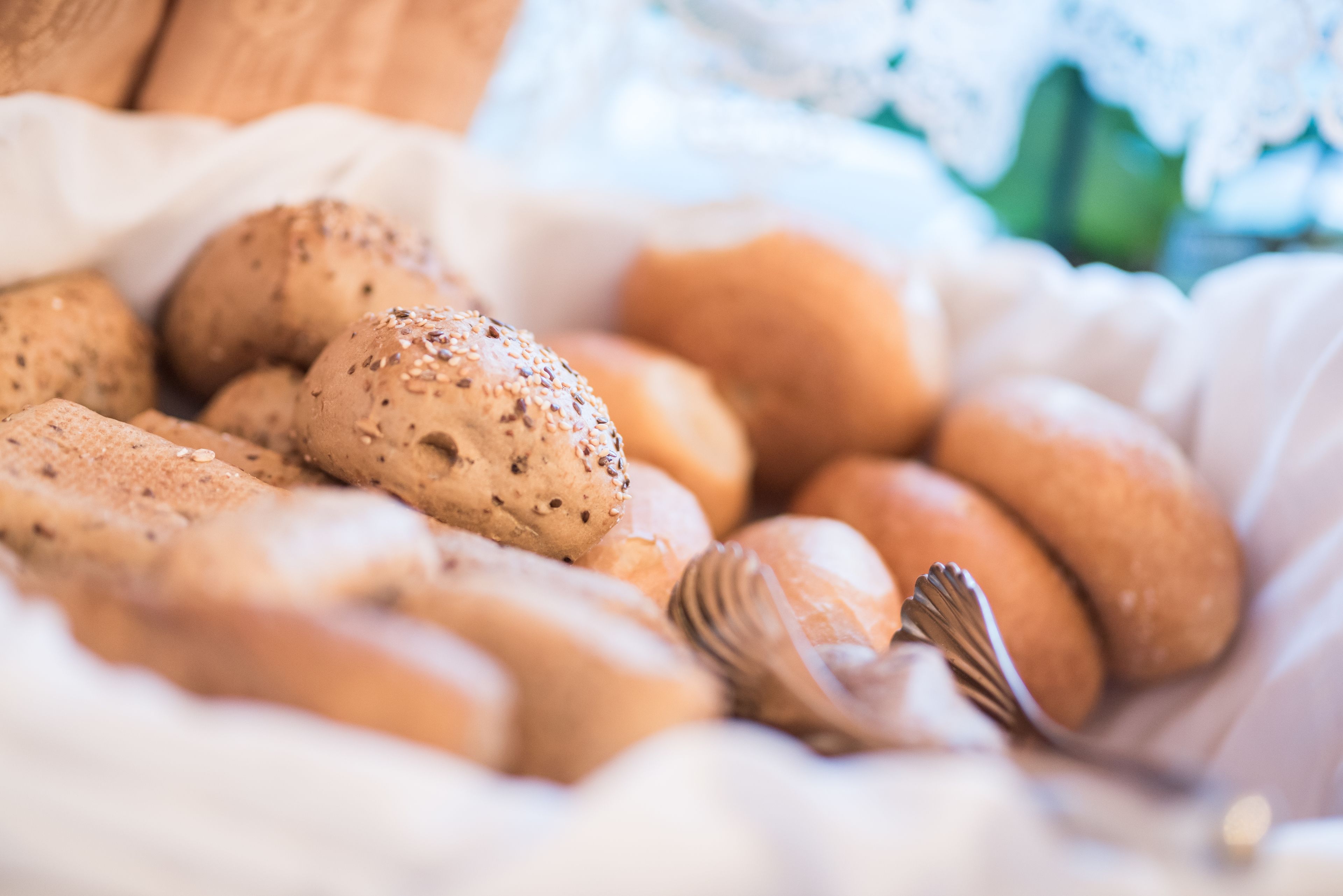 Ein Korb mit verschiedenen Brötchen, manche mit Samen, auf einem weißen Tuch.