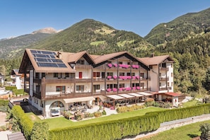Een hotel met meerdere verdiepingen, balkons, zonnepanelen en een bergachtige achtergrond.
